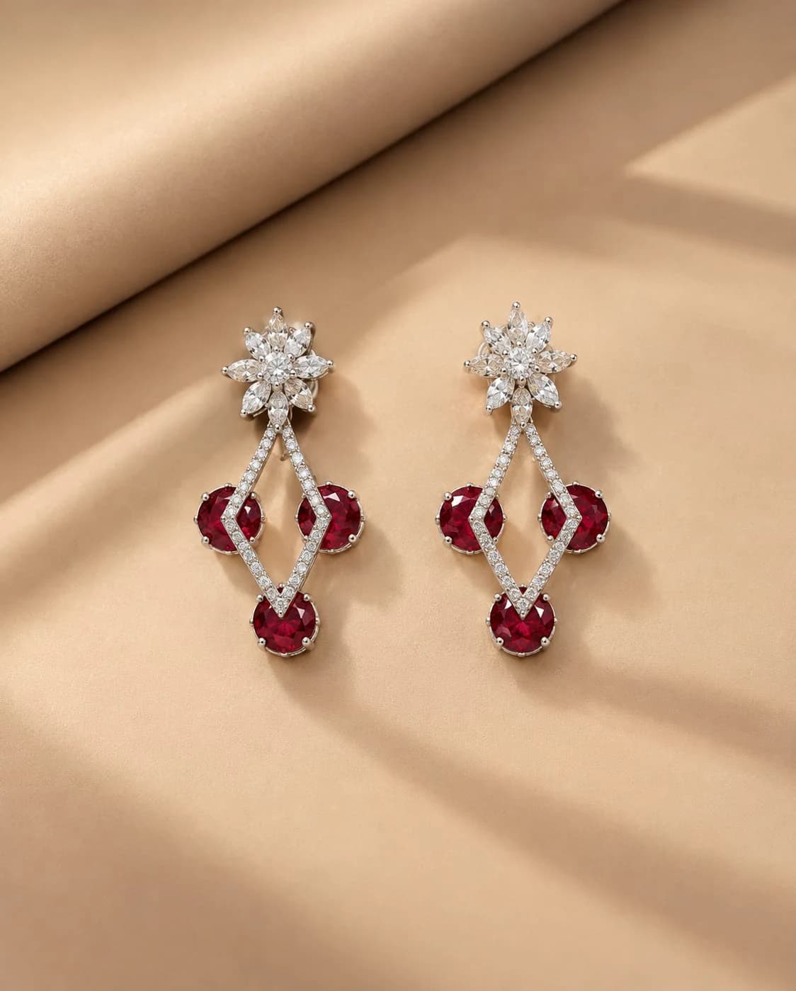 Crimson drop earrings with white floral tops and open diamond-shaped links on a warm beige set